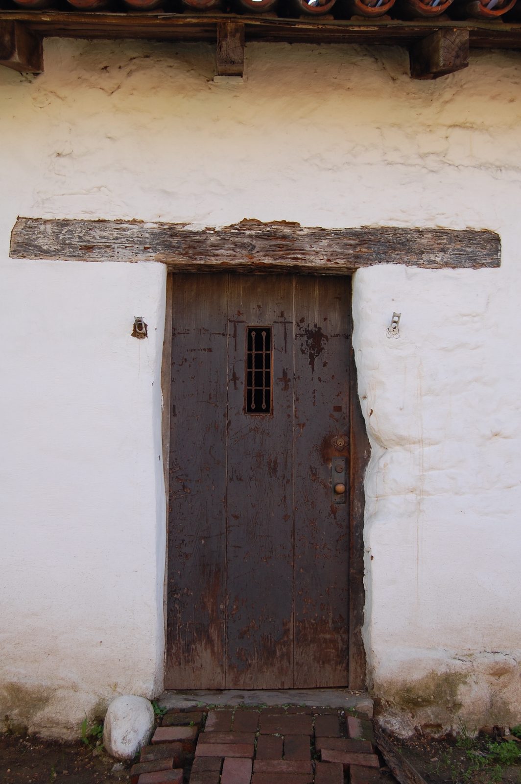 An old wooden door set into a whitewashed adobe wall beneath clay roof tiles