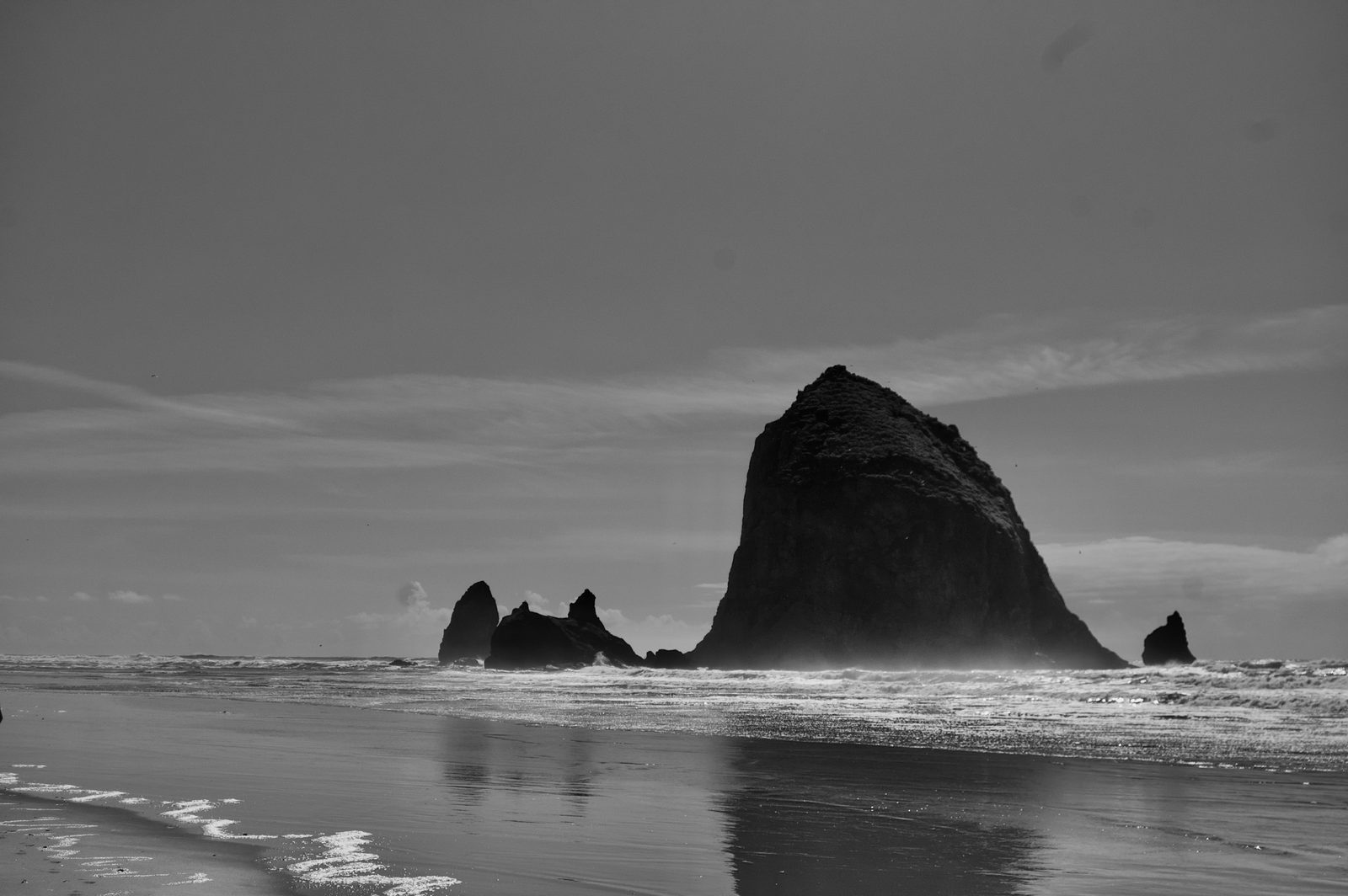 Black-and-white view of a towering sea stack rising from a misty beach at low tide