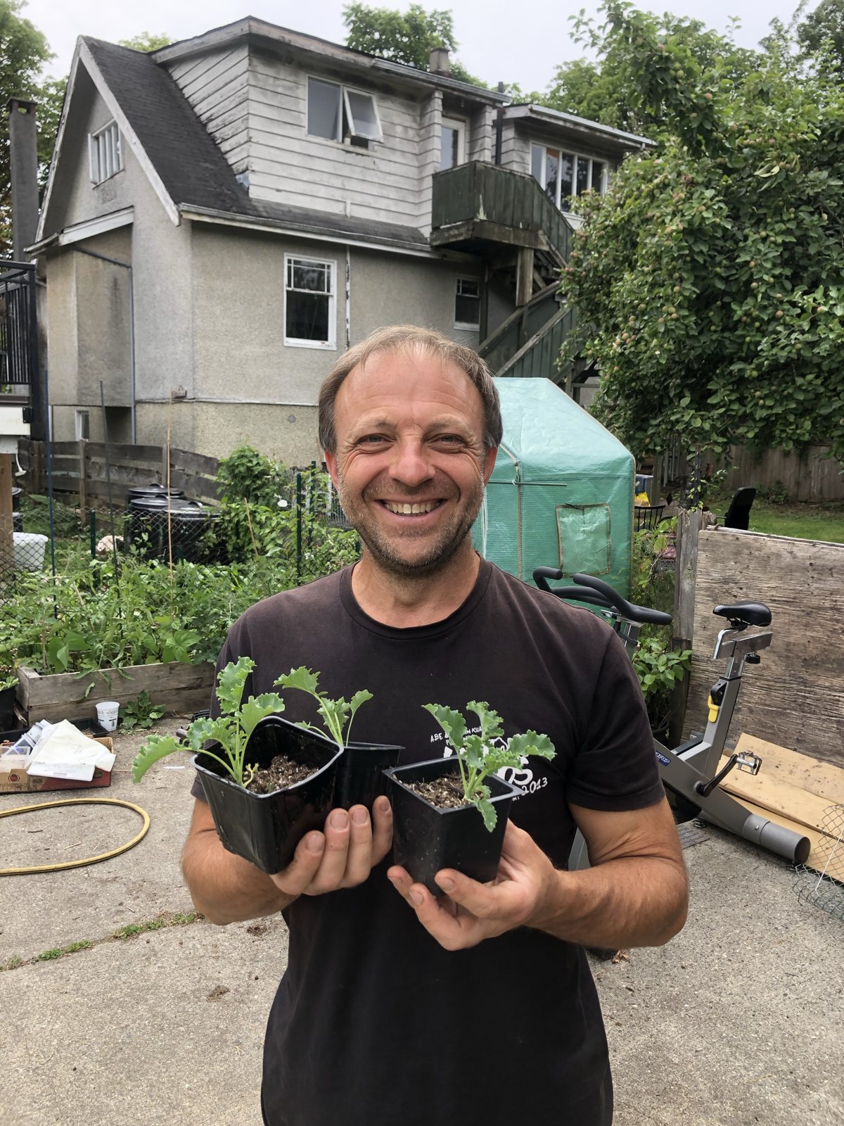 A smiling neighbour holding two kale seedlings in a backyard garden