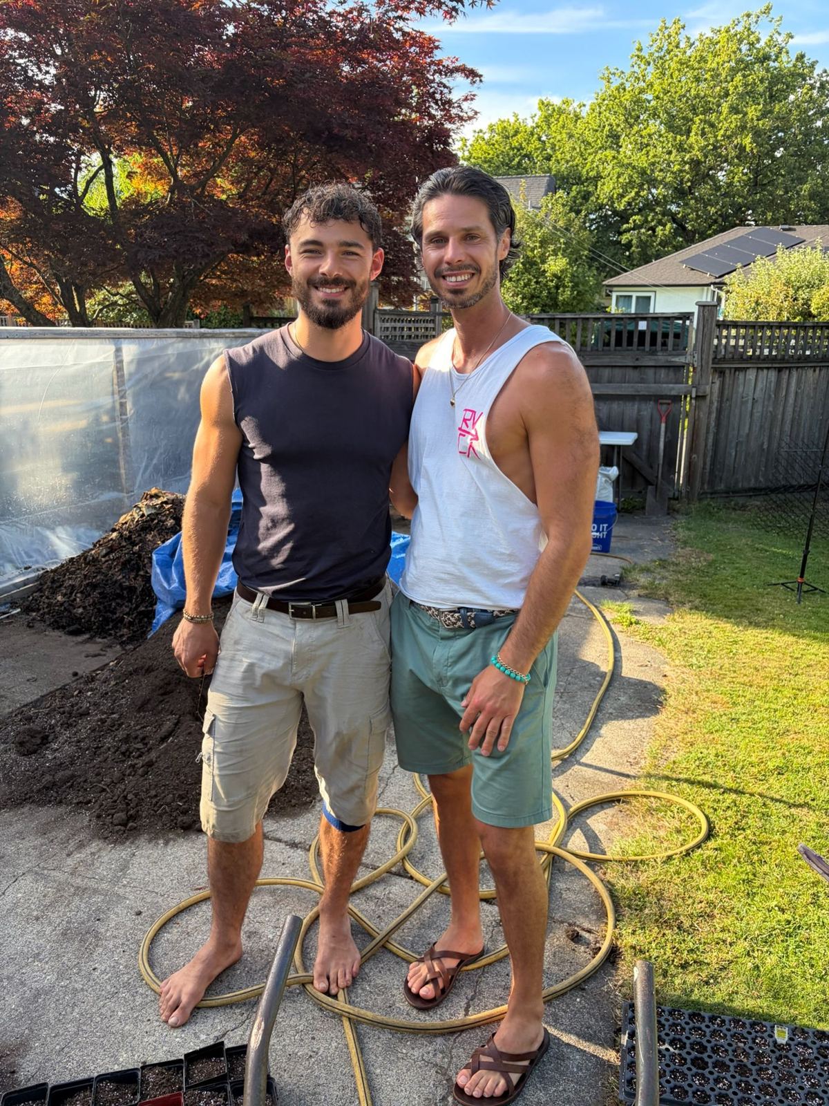 Nathan and a friend standing barefoot beside a pile of compost on a sunny day