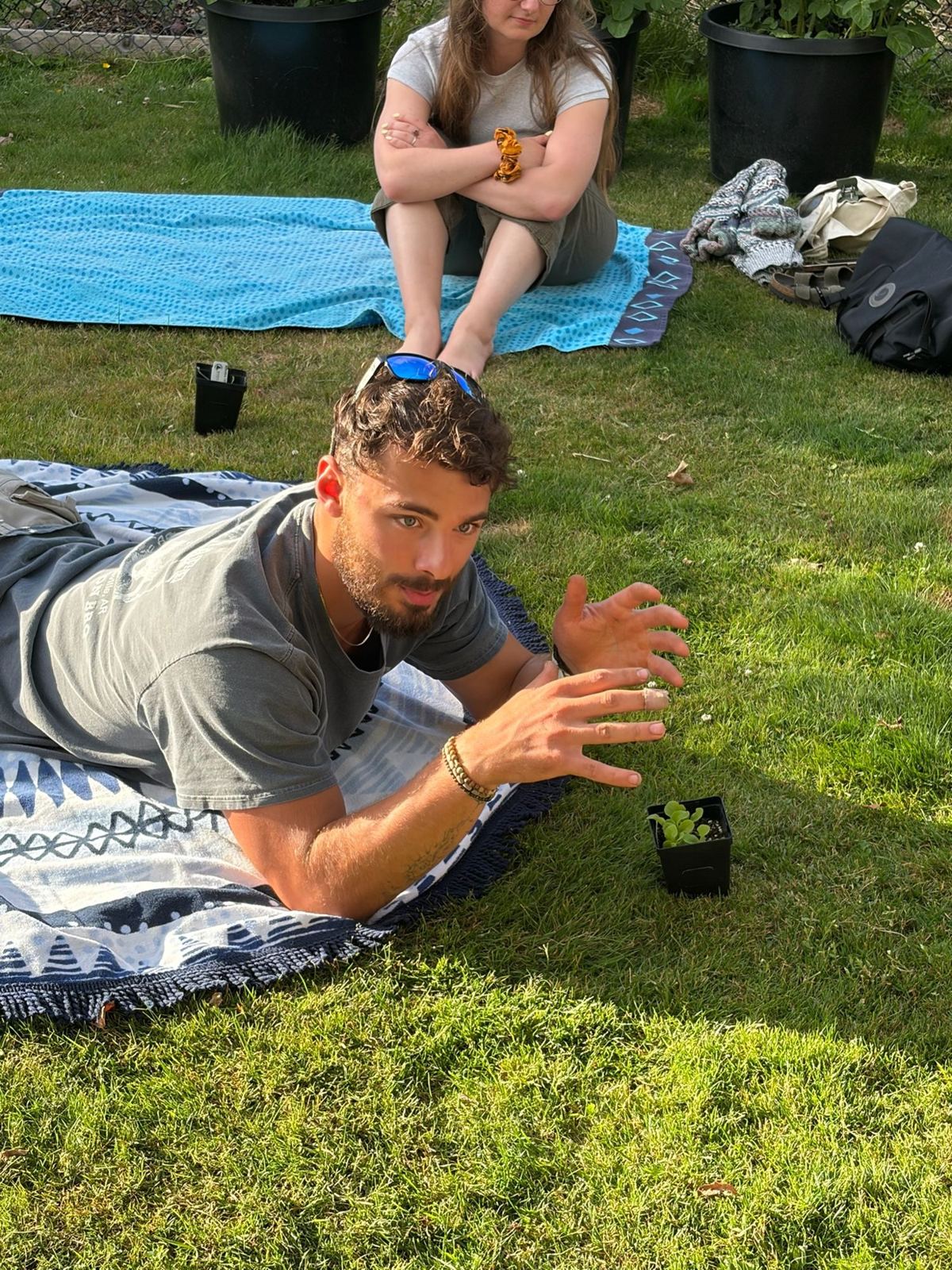 Nathan lying on a blanket in the grass, explaining something with his hands beside a seedling
