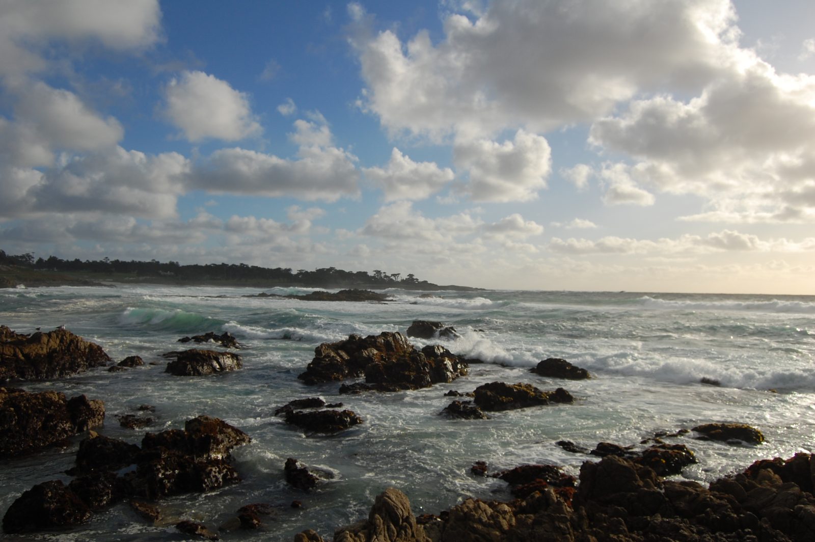 Dark rocks scattered along a wave-washed shoreline beneath a cloud-filled sky