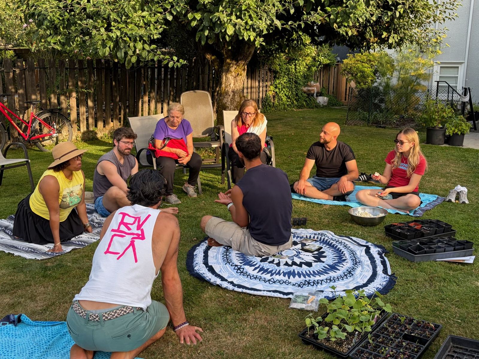 Workshop participants sitting in a circle on blankets with seed trays and seedlings