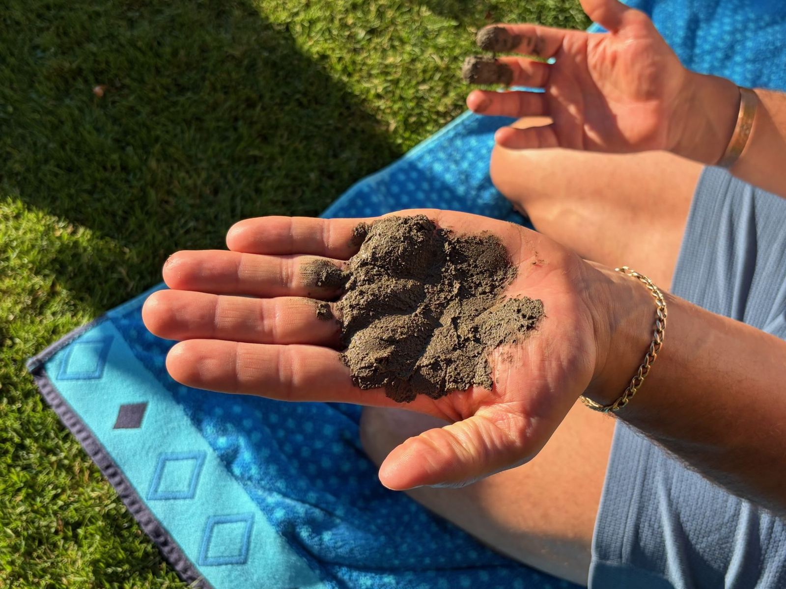 An open palm holding a clump of soil above a blanket