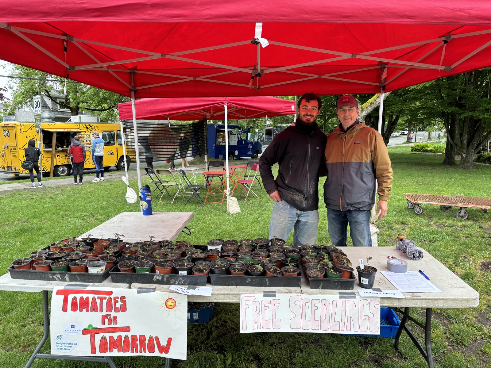 Nathan and a volunteer standing behind the Tomatoes for Tomorrow free seedling table
