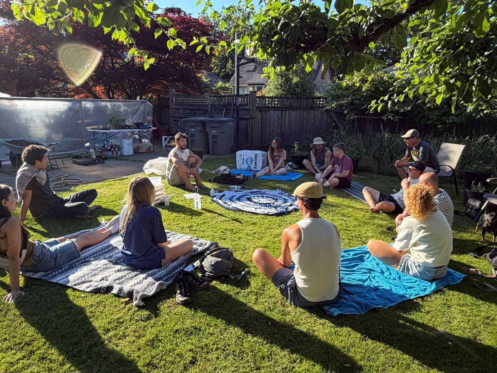Wide view of a garden workshop with people seated on blankets across the lawn