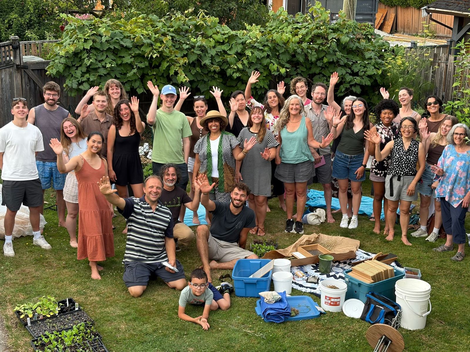 A large, joyful group photo of workshop participants with arms raised in a garden